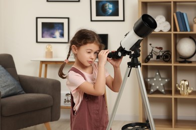 Photo of Cute little girl looking at stars through telescope in room