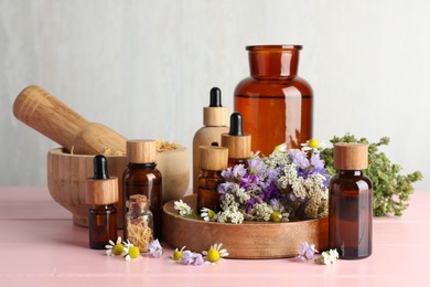 Aromatherapy. Different essential oils, mortar, pestle and flowers on pink wooden table