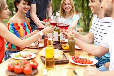 Photo of Young people with glasses of wine at table outdoors. Summer barbecue