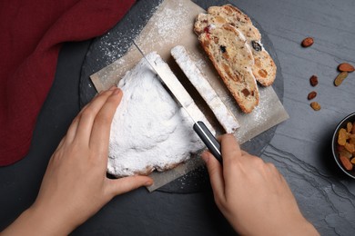 Photo of Woman cutting traditional Christmas Stollen at black table, top view