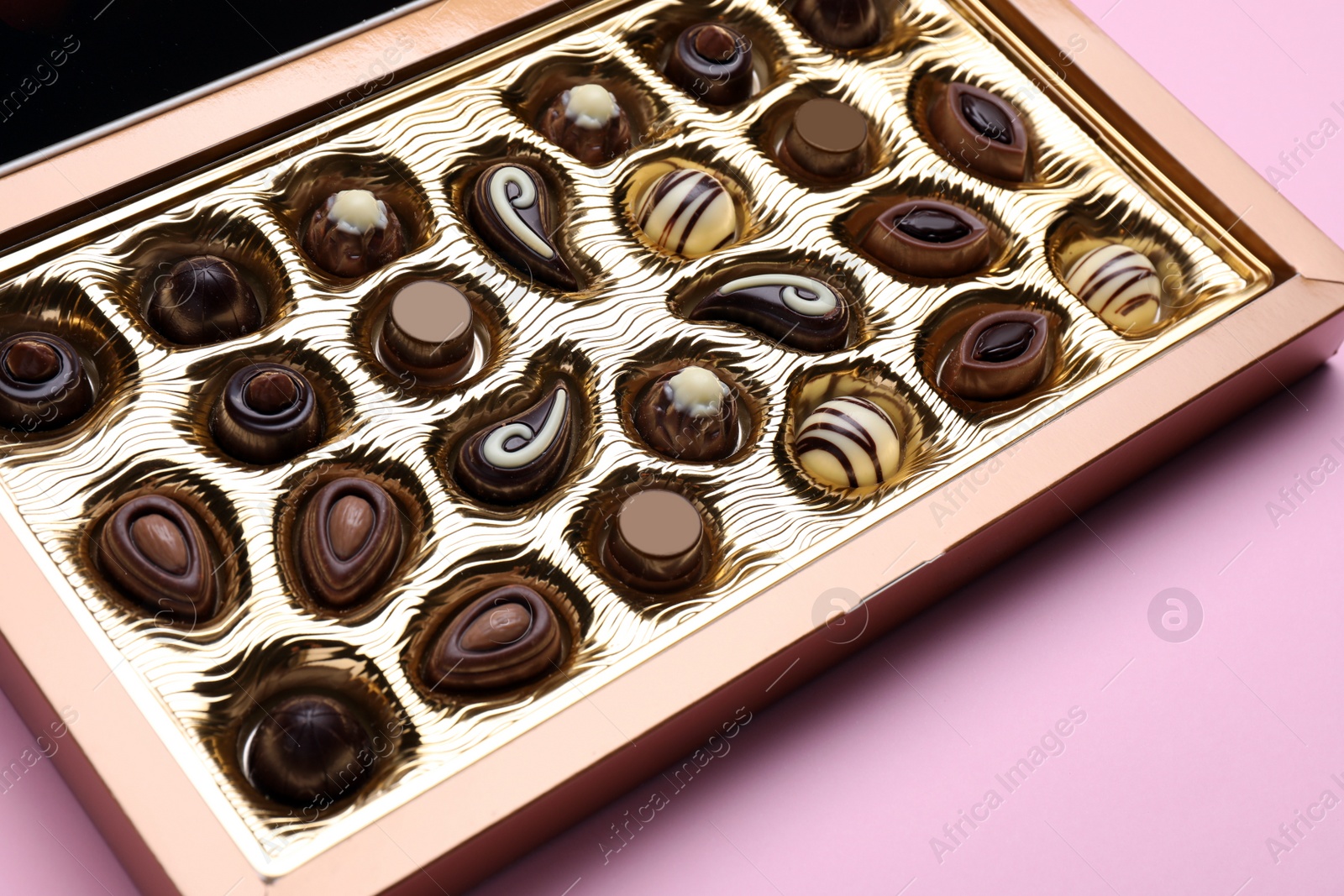 Photo of Box of delicious chocolate candies on pink background, closeup