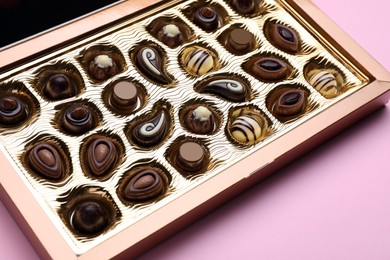 Photo of Box of delicious chocolate candies on pink background, closeup