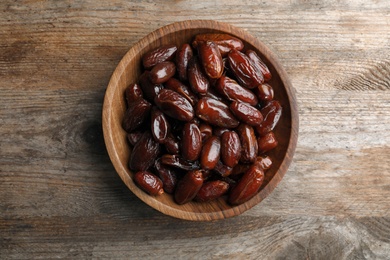 Photo of Bowl with sweet dates on wooden background, top view. Dried fruit as healthy snack