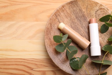 Photo of Lip balms and branches on wooden background, top view. Space for text