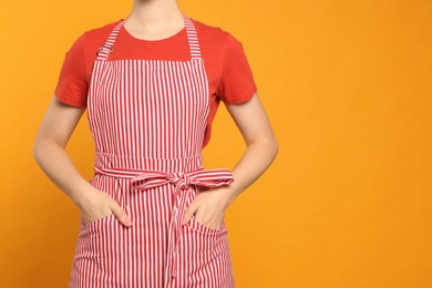 Photo of Woman in clean striped apron on orange background, closeup