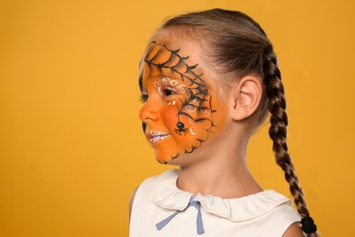 Cute little girl with face painting on orange background