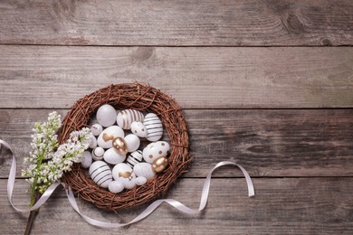 Photo of Many painted Easter eggs, branchlilac flowers and ribbon on wooden table, flat lay. Space for text