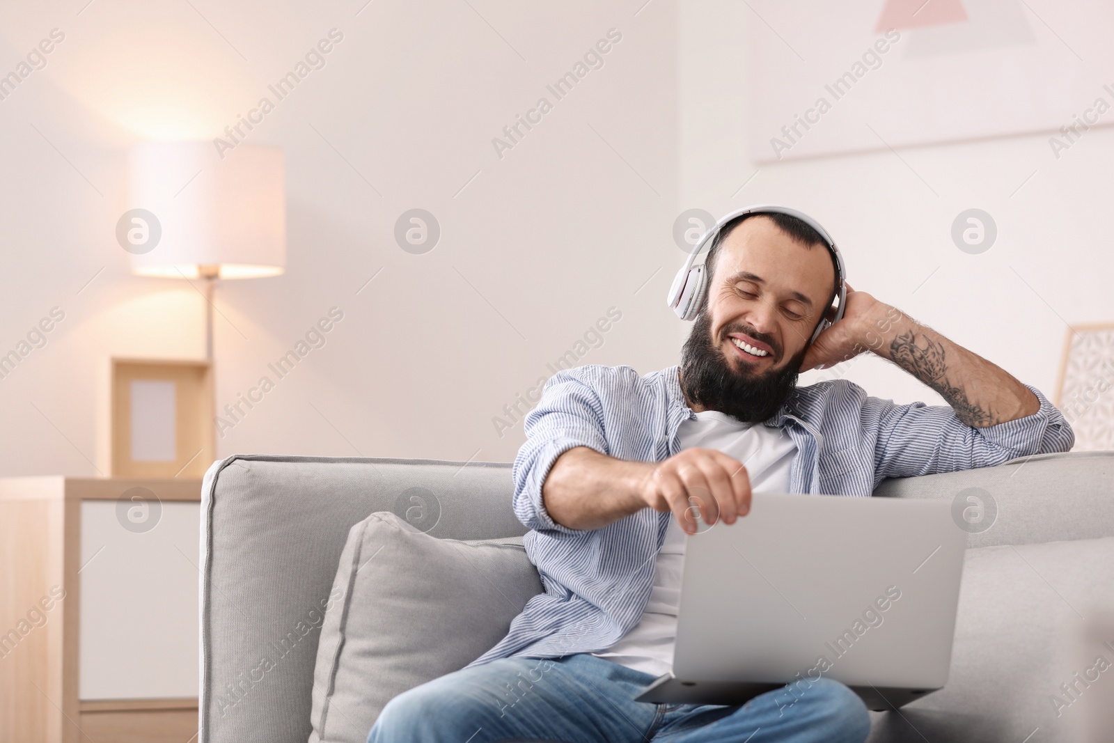 Photo of Mature man with headphones and laptop on sofa at home