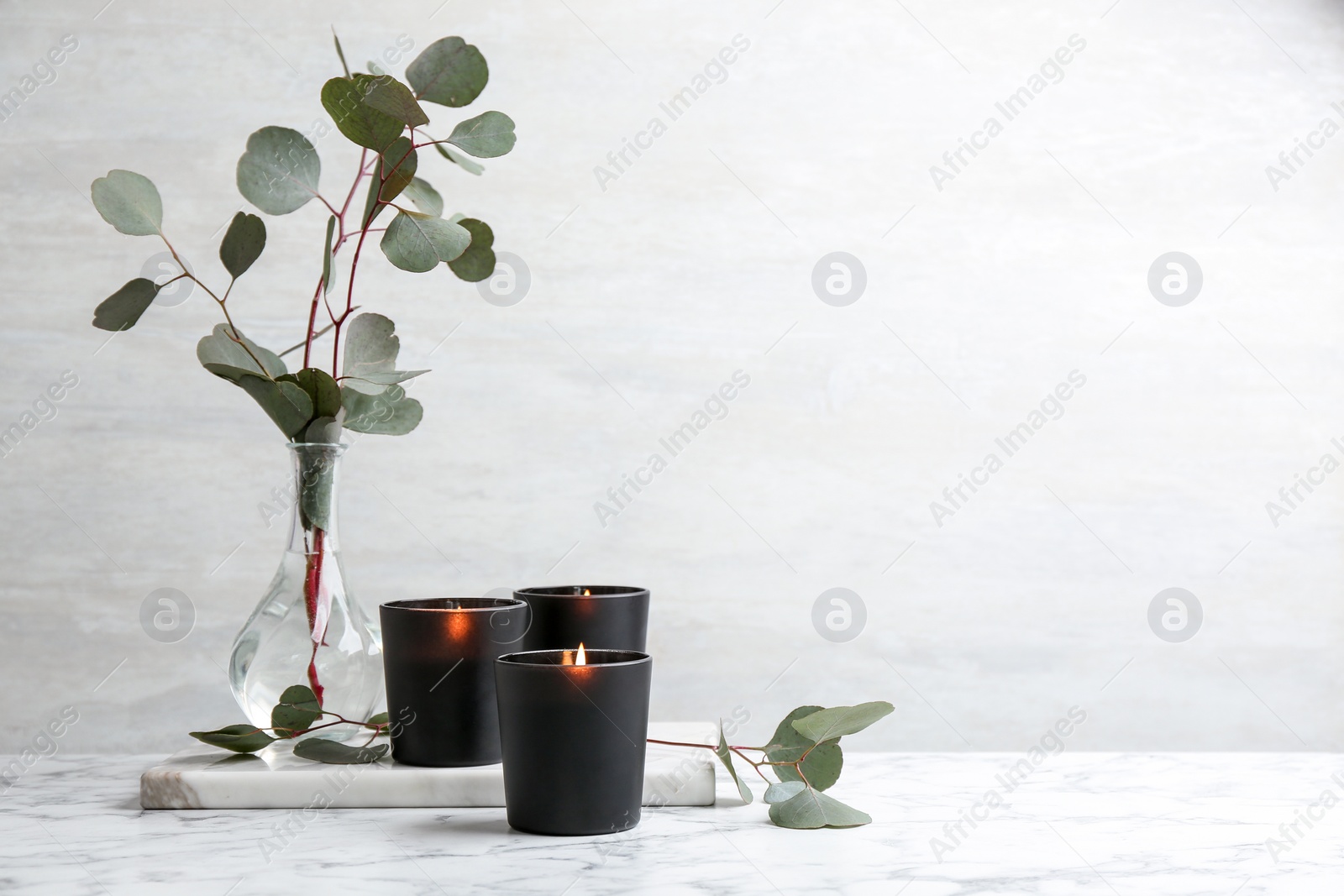 Photo of Burning candles and green branches on marble table, space for text