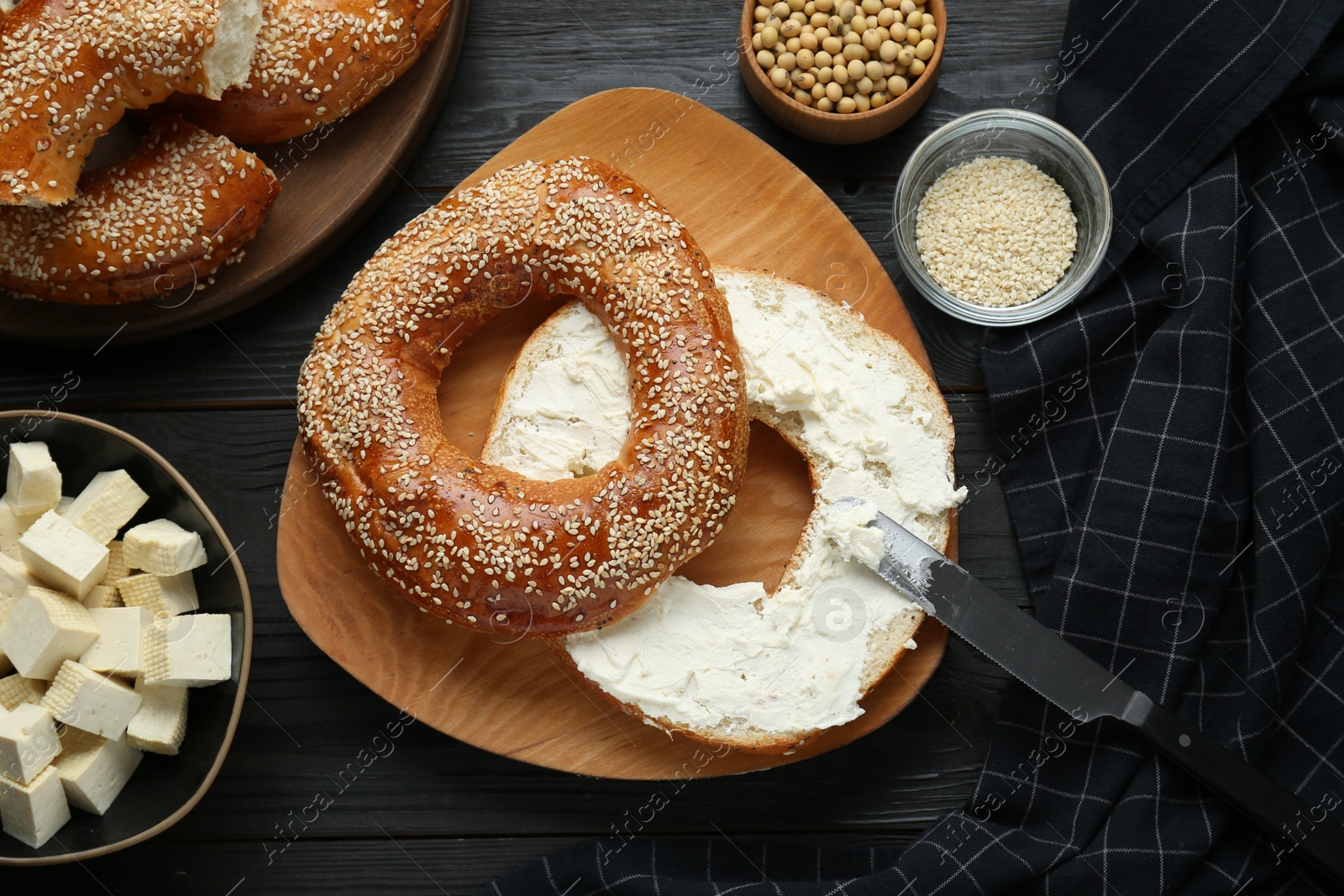 Photo of Delicious bagel with tofu cream cheese and soy beans on black wooden table, flat lay