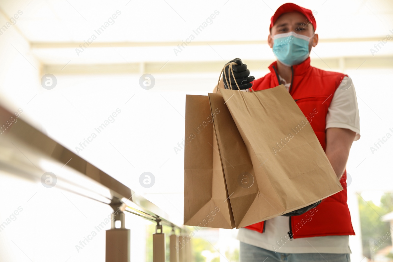 Photo of Courier in protective mask and gloves with order indoors. Restaurant delivery service during coronavirus quarantine