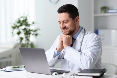 Photo of Smiling doctor having online consultation via laptop at table in clinic