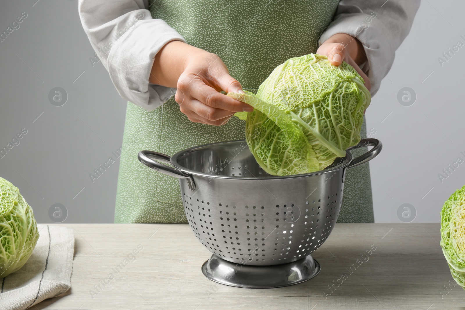 Photo of Woman separate leaf from fresh savoy cabbage at wooden table, closeup