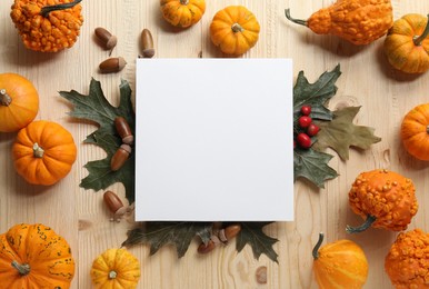 Thanksgiving day. Flat lay composition with pumpkins and blank card on light wooden table, space for text