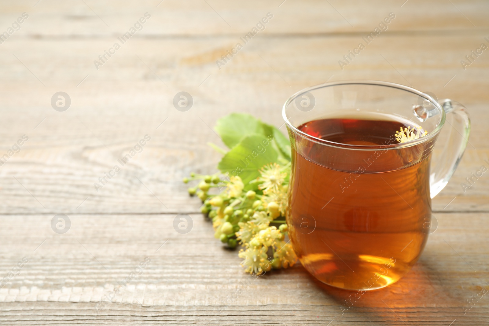 Photo of Cup of tea and linden blossom on wooden table. Space for text