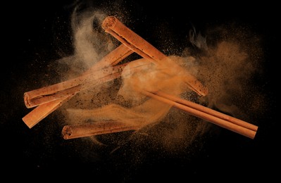 Image of Aromatic cinnamon sticks and powder flying on black background