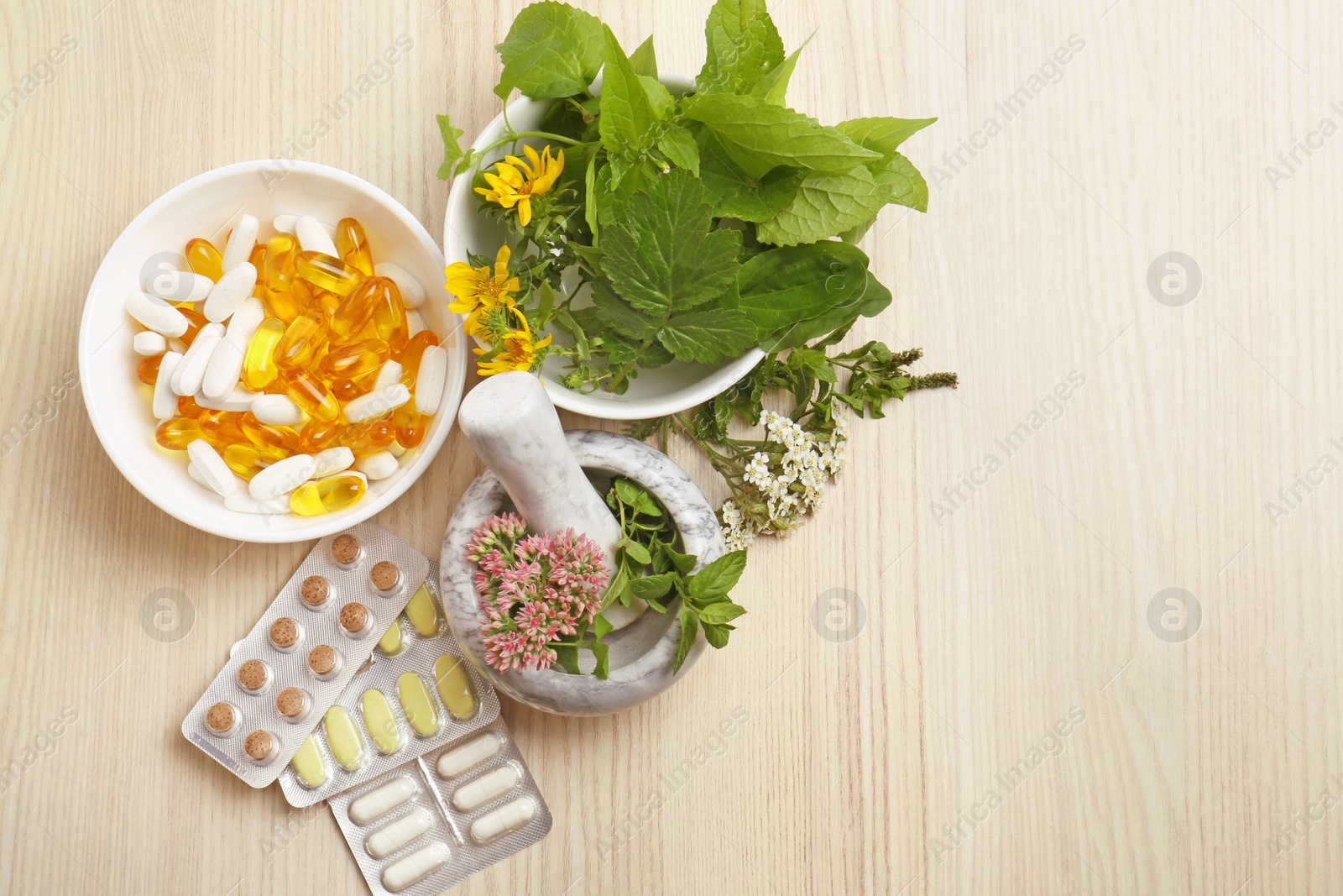 Photo of Mortar with fresh herbs and pills on wooden table, flat lay. Space for text