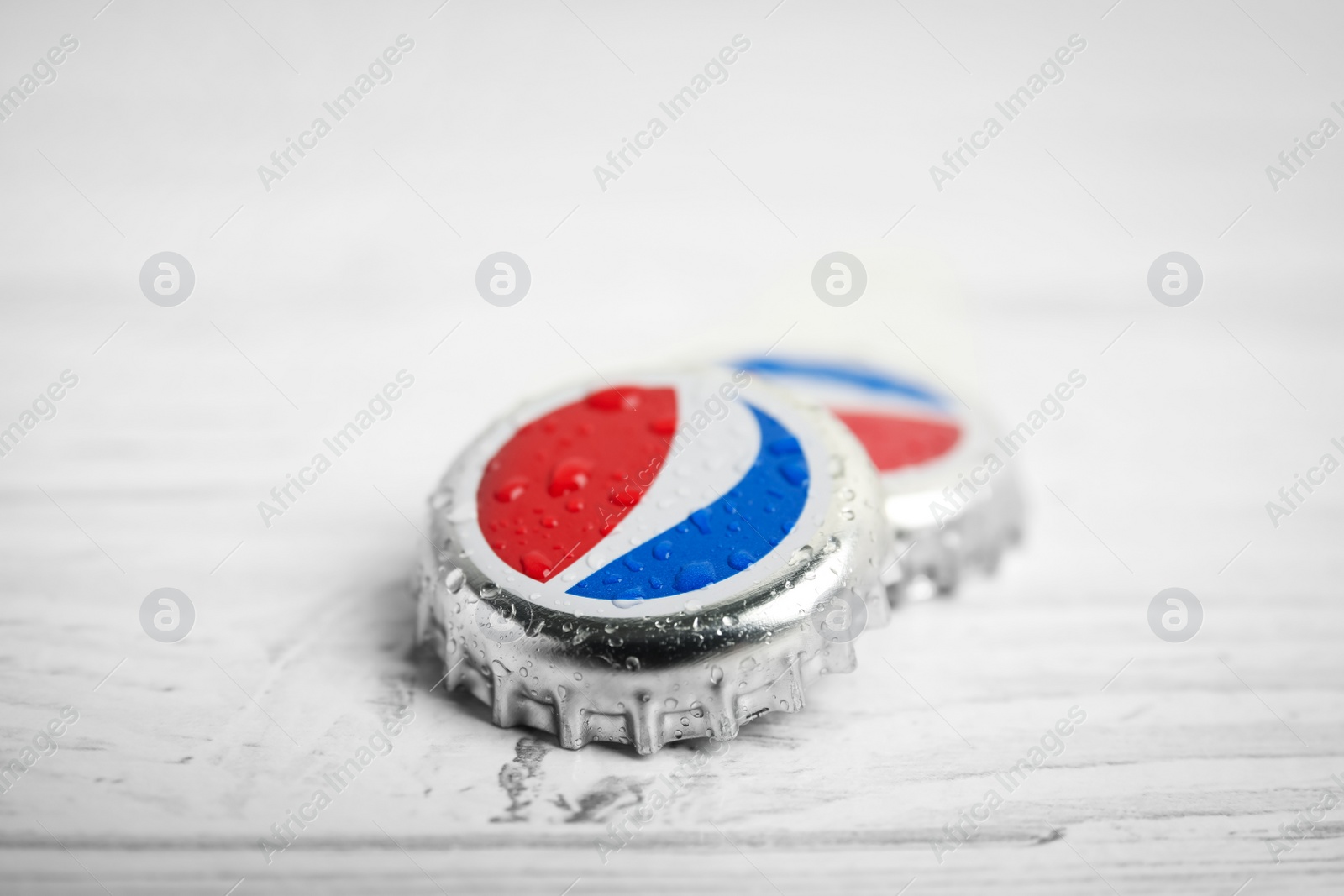 Photo of MYKOLAIV, UKRAINE - FEBRUARY 11, 2021: Pepsi lids with water drops on white wooden table, closeup