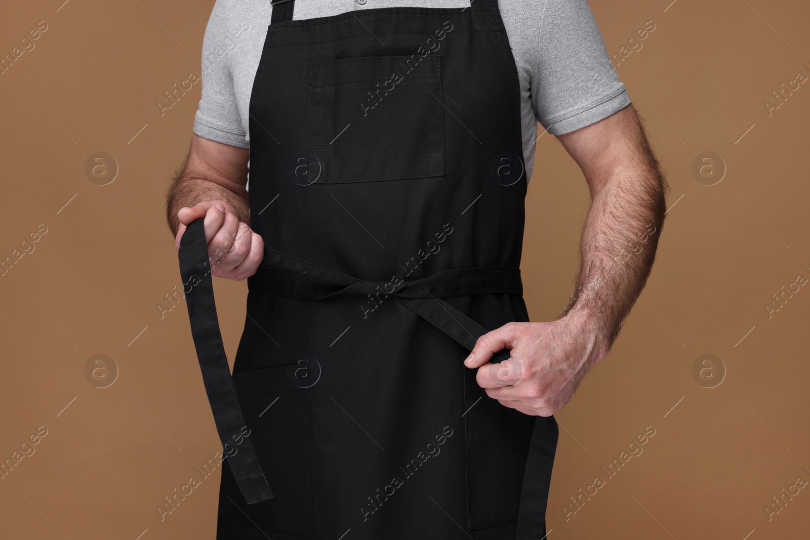 Photo of Man wearing kitchen apron on brown background, closeup. Mockup for design