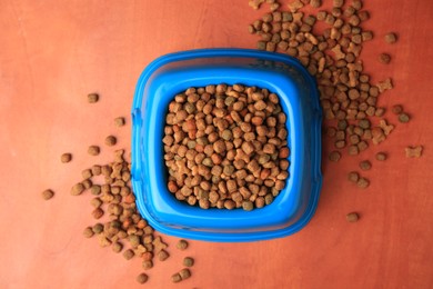 Dry pet food in feeding bowl on orange background, flat lay