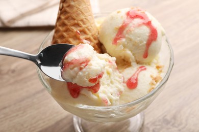 Photo of Taking tasty vanilla ice cream with strawberry topping from glass dessert bowl on table, closeup