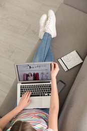 Woman holding laptop with open beauty blogger site on sofa, above view