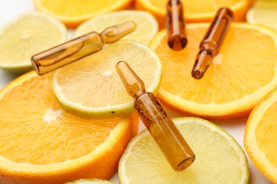 Photo of Skincare ampoules with vitamin C, lemon and orange slices on white background, closeup