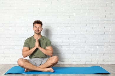 Young man practicing zen yoga near white brick wall, space for text