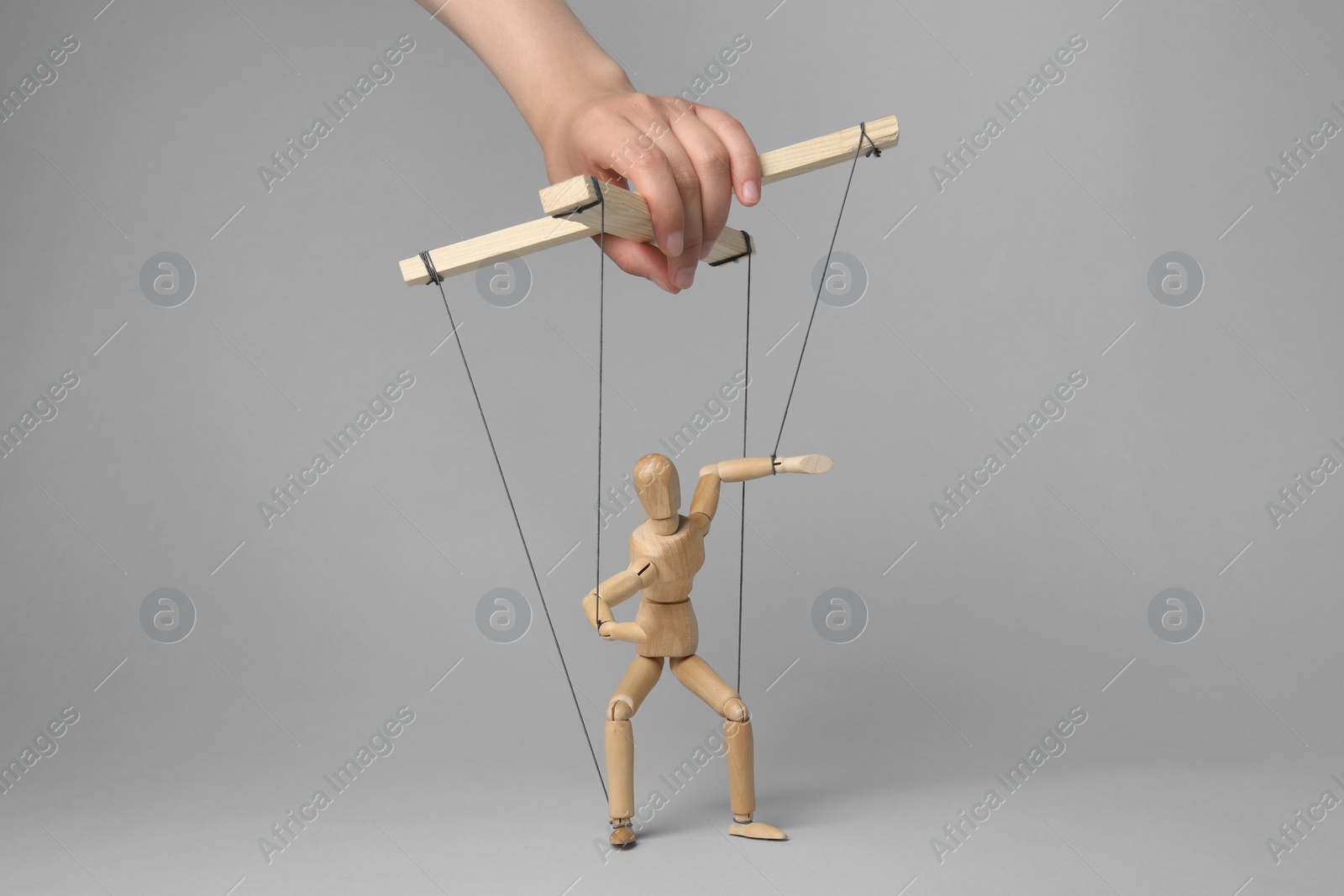 Photo of Woman pulling strings of puppet on light grey background, closeup