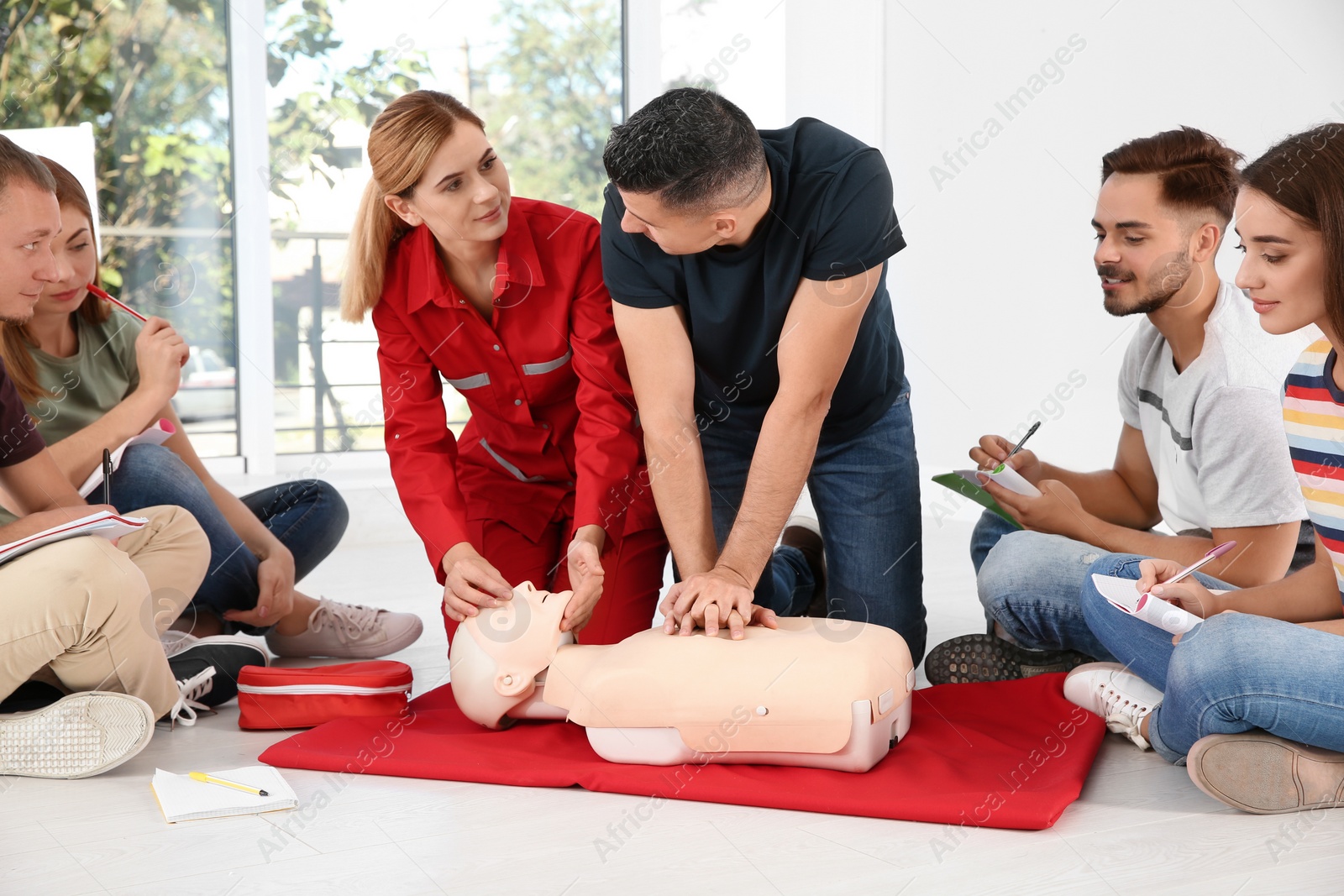 Photo of Group of people with instructor practicing CPR on mannequin at first aid class indoors