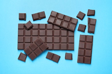 Pieces of delicious chocolate bars on light blue background, flat lay