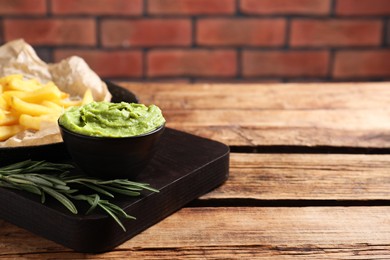 Photo of Serving board with parchment, french fries, avocado dip and rosemary on wooden table, space for text