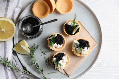 Plate of delicious tartlets with black caviar, cream cheese and lemon served on white wooden table, top view