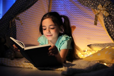 Photo of Little girl reading fairy tale in play tent at home