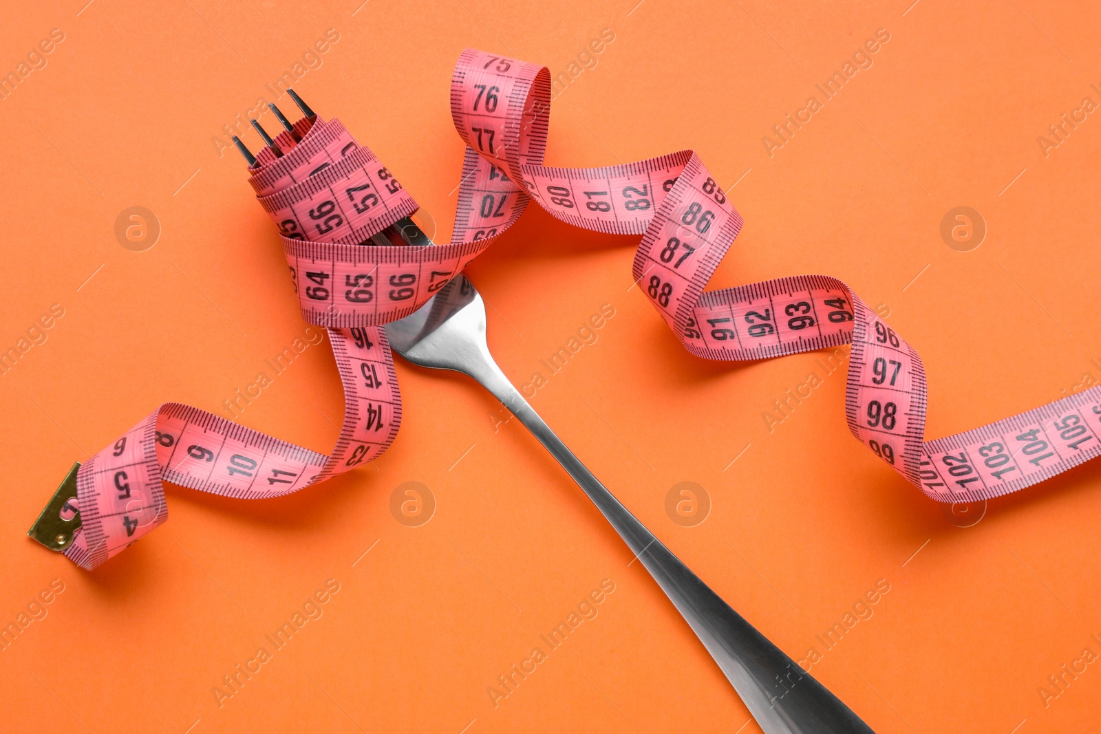 Photo of Fork with measuring tape on orange background, top view. Diet concept