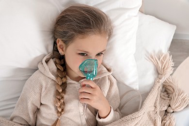 Little girl using nebulizer for inhalation on bed indoors, top view