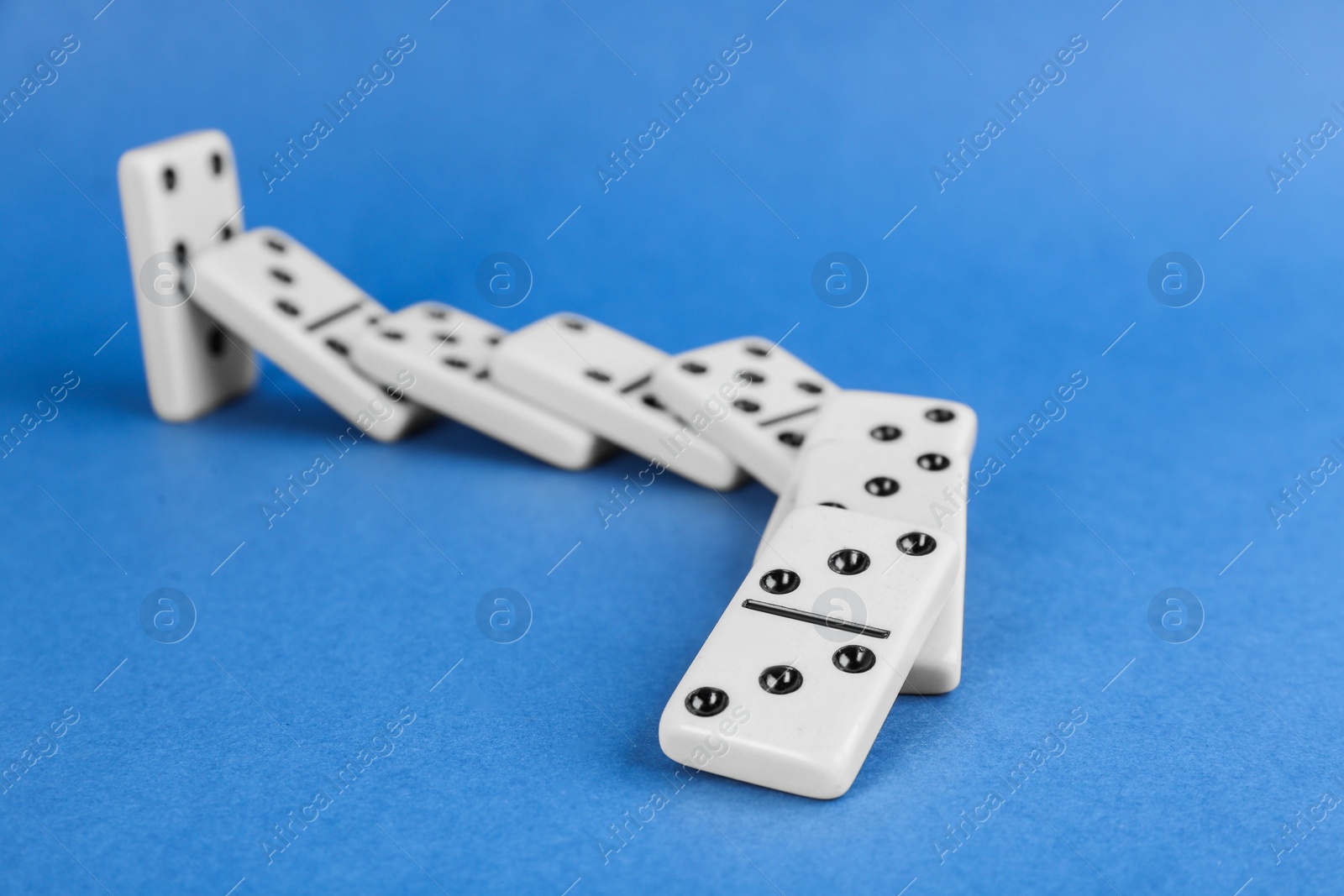 Photo of White domino tiles falling on blue background