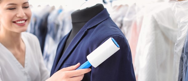 Image of Young woman removing dust from jacket with lint roller, banner design. Dry-cleaning service
