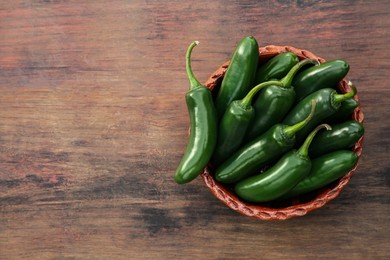 Photo of Bowl with green jalapeno peppers on wooden table, top view. Space for text