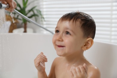 Photo of Mother washing her little son's hair from shampoo in bathroom, closeup