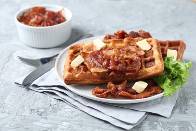 Delicious Belgium waffles served with fried bacon and butter on grey table, closeup