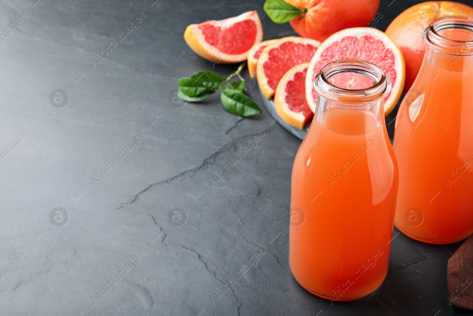 Photo of Tasty freshly made grapefruit juice on black table. Space for text