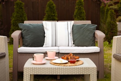 Outdoor breakfast with tea and croissants on rattan table in garden