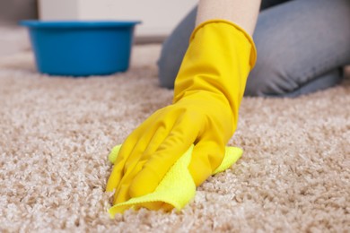 Photo of Woman in rubber gloves cleaning carpet with rag indoors, closeup