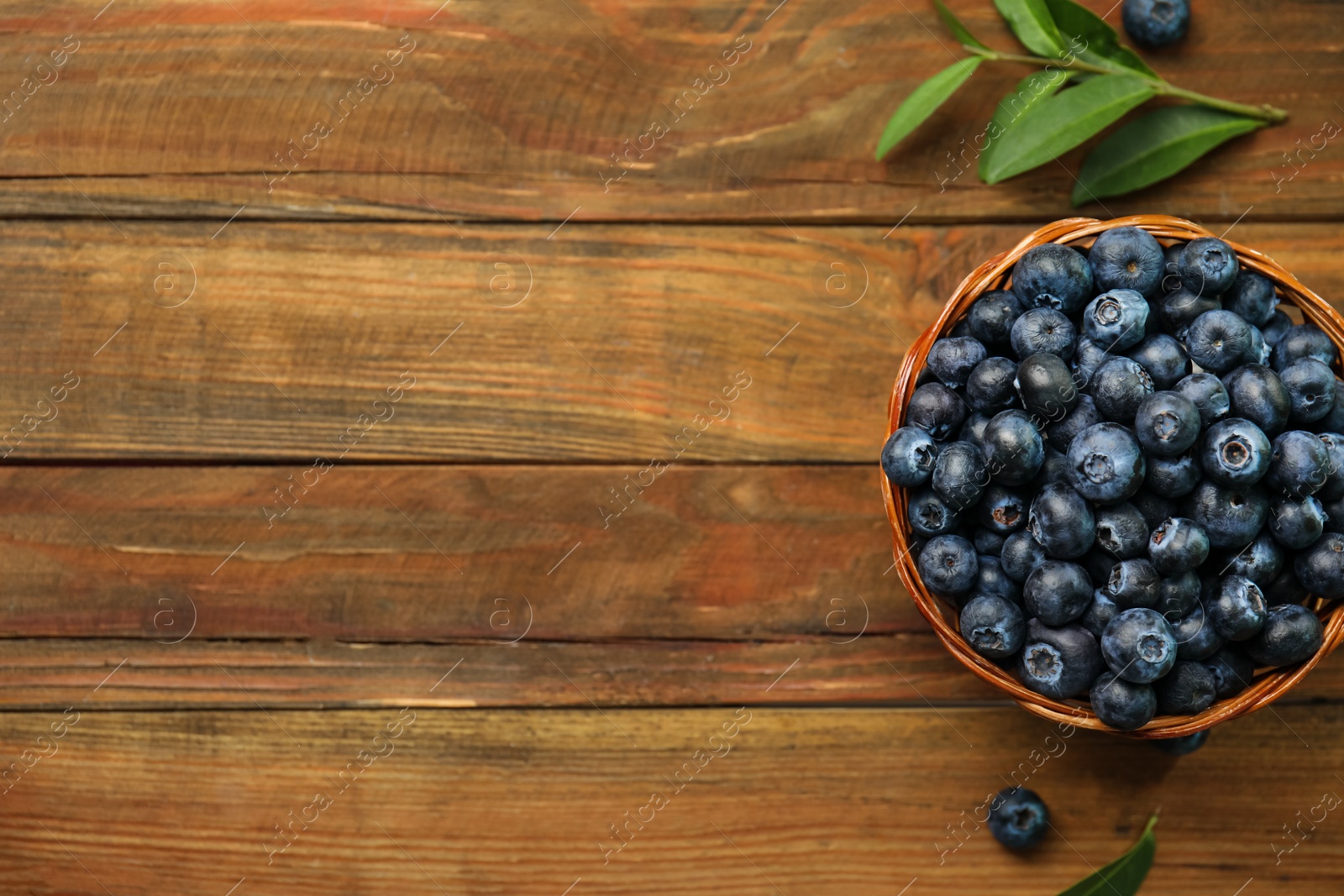 Photo of Tasty ripe blueberries in wicker bowl on wooden table, flat lay. Space for text