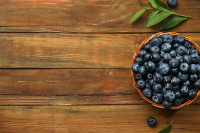 Tasty ripe blueberries in wicker bowl on wooden table, flat lay. Space for text