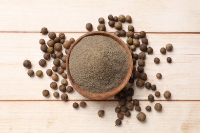 Photo of Ground and whole allspice berries (Jamaica pepper) in bowl on light wooden table, top view