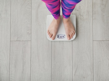 Woman measuring her weight using scales on floor, top view. Healthy diet