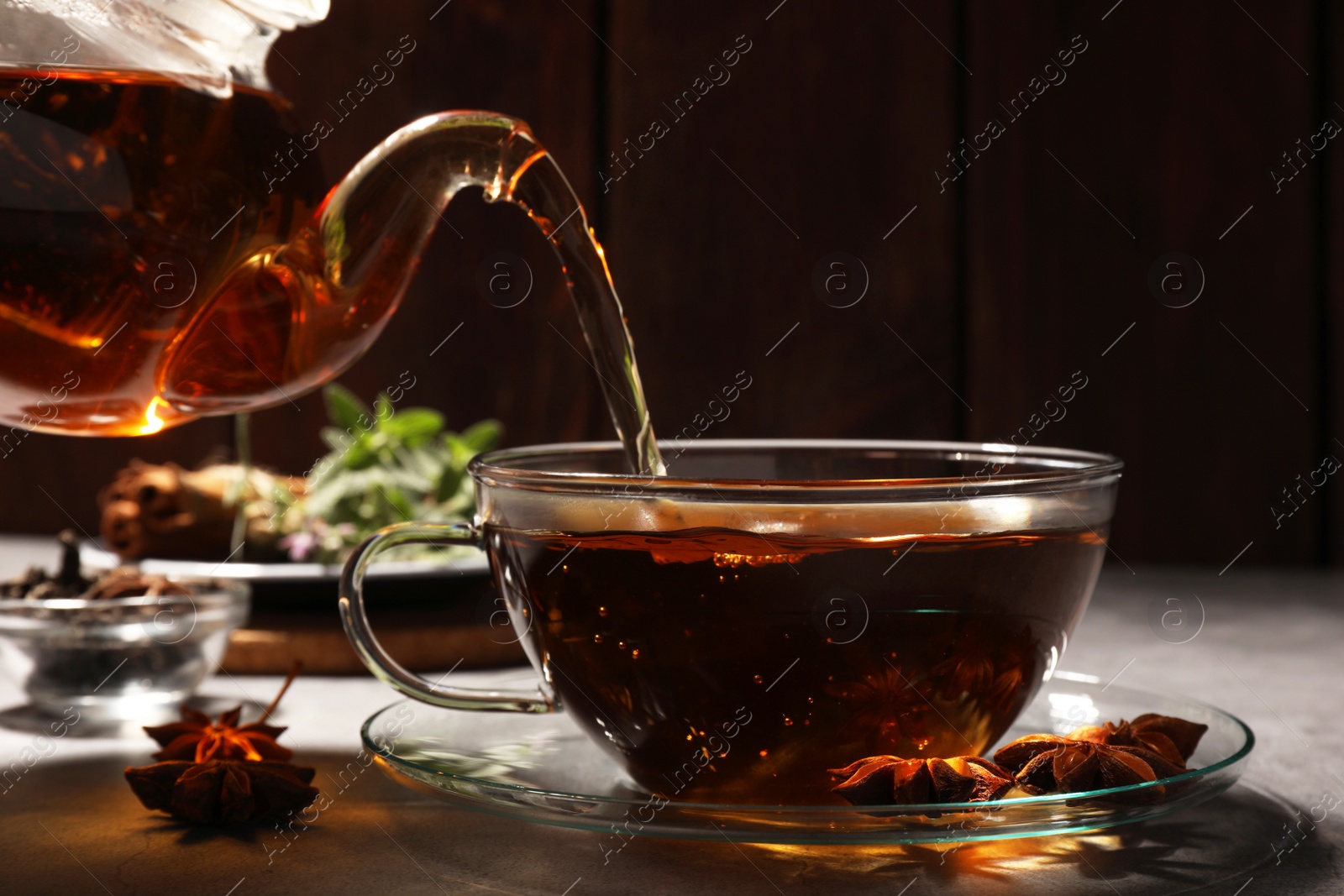 Photo of Pouring aromatic anise tea from teapot into glass cup on light grey table