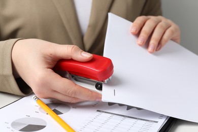 Photo of Woman stapling papers at white table indoors, closeup